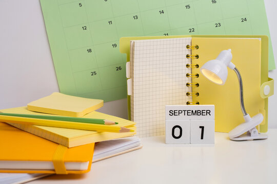 Wooden block calendar showing September 01 illuminated by a small lamp next to school stationery and notebooks