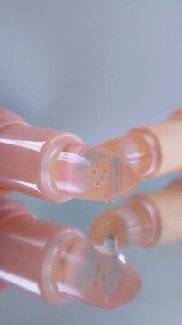 Extreme front close up of two lip balm products with transparent tips. Clear liquid droplets being dispensed. Cosmetic products neatly arranged on glass surface for beauty concept.
