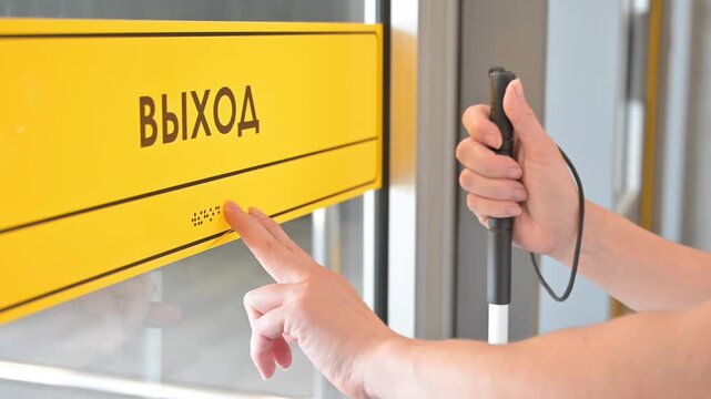 A blind woman reads a braille sign on a door. Exiting the metro.