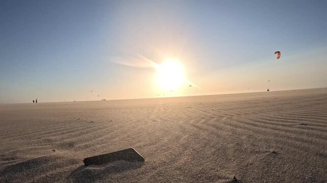 Smartphone resting on the sandy beach at Kijkduin with colorful kitesurfers in the background during sunset