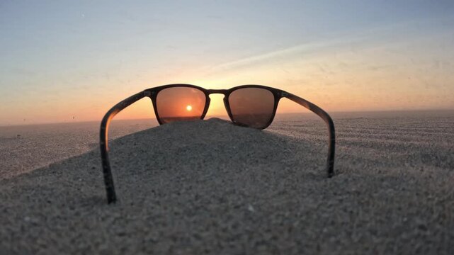 Dramatic coastal sunset with sunglasses framed against the North Sea and distant kitesurfers
