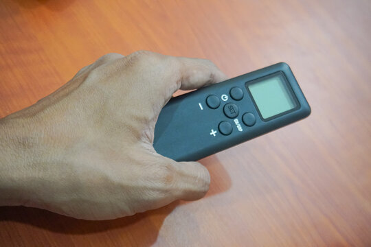 Person Holding Black Wireless Remote Control On Wooden Table