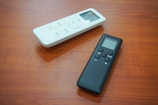Two Black And White Remote Controls On Wooden Table
