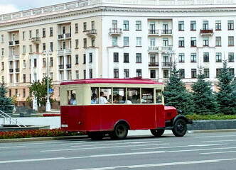 Obraz premium Vintage red and cream retro bus with tourists driving on Independence avenue in Minsk Belarus for historical city excursion banner post-soviet travel guide and transport heritage poster design