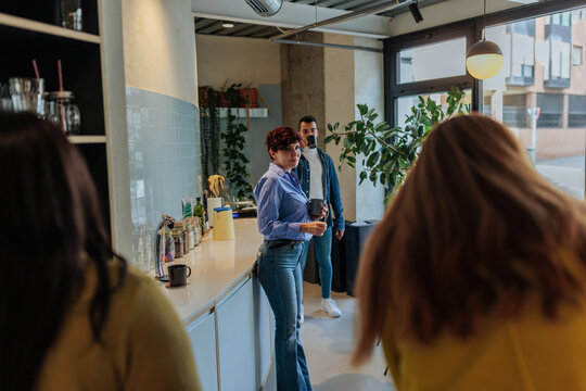 Coworkers socializing during coffee break in modern office kitchen