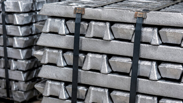 Close up of stacked silver metal ingots secured with black straps. Raw aluminum or zinc bars in an industrial warehouse. Metallurgy and manufacturing commodity concept