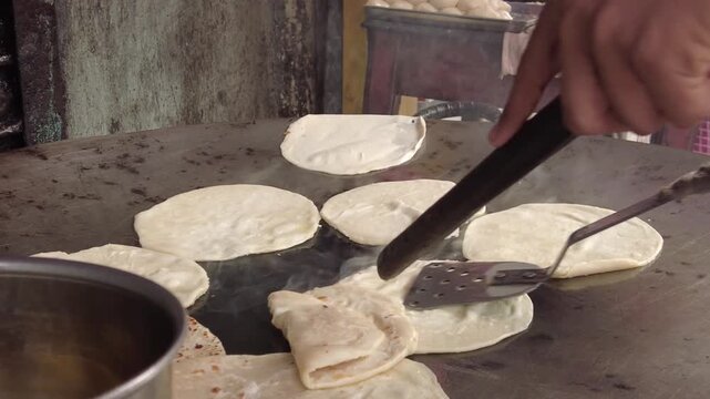 A chef skillfully prepares traditional Indian flatbread, called chapati or roti, on a large, sizzling hot plate, demonstrating the age-old culinary art of bread making