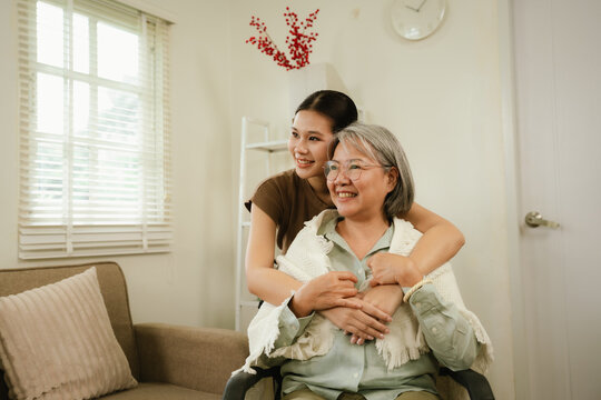 Young caregiver warmly hugging a smiling senior woman at home, expressing love, comfort, trust, and compassionate elderly care.