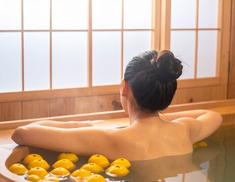Rear view of a woman relaxing in a traditional Japanese hinoki wooden bathtub with floating yuzu citrus, winter solstice hot bath