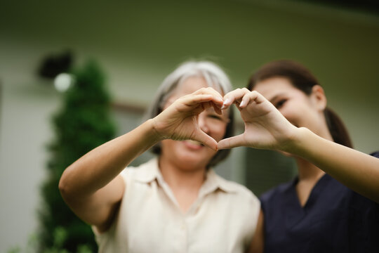 Smiling senior woman and caregiver making a heart shape with their hands, expressing love, trust, compassion, and quality elderly care.