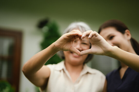 Smiling senior woman and caregiver making a heart shape with their hands, expressing love, trust, compassion, and quality elderly care.