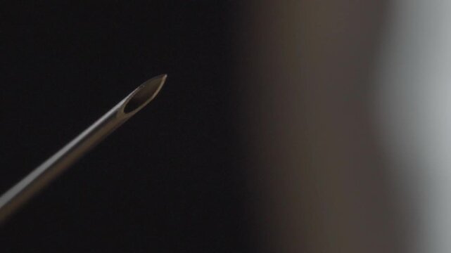 Macro closeup showing sterile hypodermic needle tip against dark background highlighting precision medical equipment for healthcare and clinical use