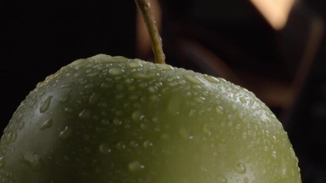 Macro closeup showing fresh green apple covered with water droplets highlighting natural texture and freshness against dark background