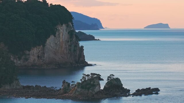 Stunning coastal landscape featuring rugged cliffs and sea stacks at Cathedral Cove, Coromandel Peninsula, New Zealand, at sunset.