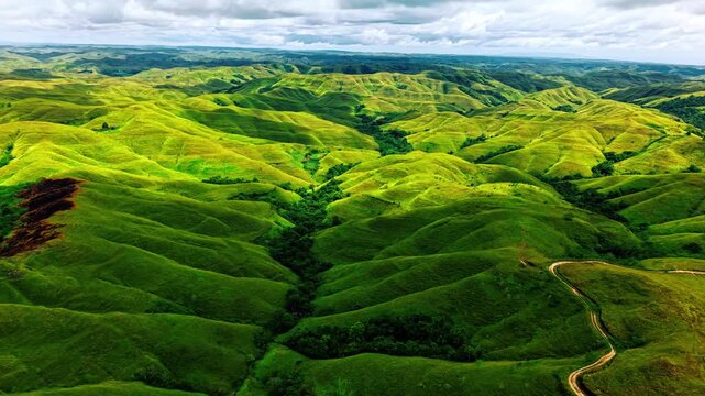 Aerial view of lush green rolling hills in vast mountain landscape during cinematic drone flight sequence.