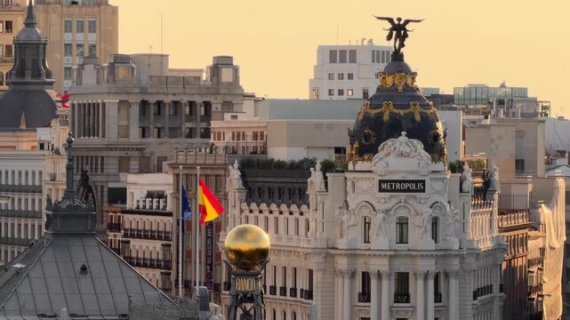 Majestic view of the Madrid skyline, showing the famous buildings and the Spanish flag waving in the wind against a warm sunset sky, showcasing the city's unique architecture
