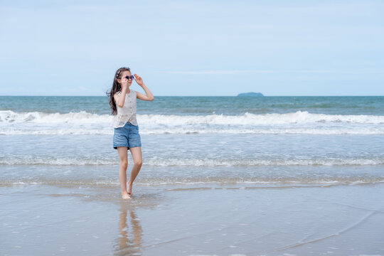 A happy young girl walks along the shoreline enjoying a peaceful summer vacation celebrating childhood freedom outdoor adventure and healthy beach lifestyle.
