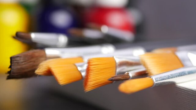 Close-up motion of various artist paintbrushes with colorful bottles in background