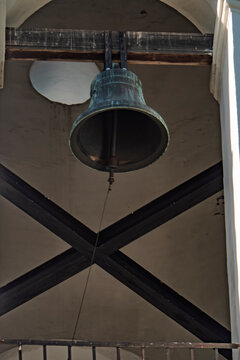 Large bronze bell hanging in a church tower with wooden beams and stone belfry interior