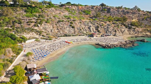 Drone view of Konnos Beach in Cyprus. Sandy bay, clear turquoise water and rugged cliffs form a beautiful Mediterranean beach scene.