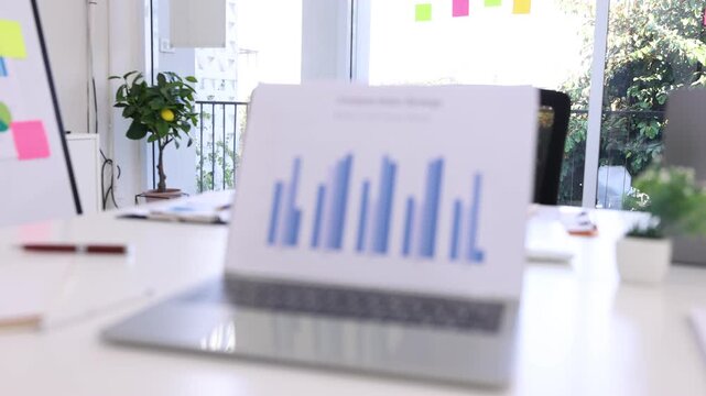A modern laptop placed on an office desk displaying a sales strategy comparison bar chart, surrounded by professional workspace elements.