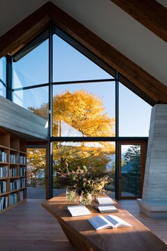 Bright loft reading nook with panoramic glass window showing golden fall tree for minimalist library background and study room design