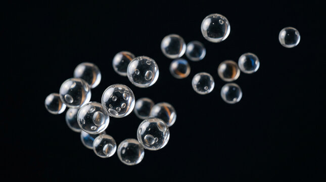 Transparent glass spheres or bubbles floating in the air against a black background, macro photography of clear round objects with internal reflections and refractions