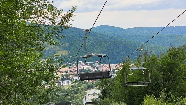 View from underneath a descending chairlift, revealing the town of Gura Humorului in the valley below surrounded by green mountain slopes.
