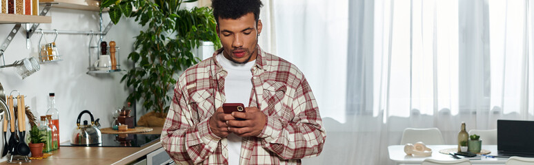 Handsome young man stands in a stylish kitchen using his smartphone and looking focused © LIGHTFIELD STUDIOS