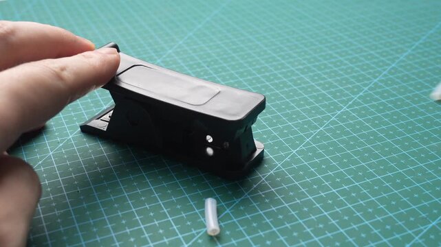 Close-up of hands using plastic tube cutter on translucent silicone tubing over green cutting mat