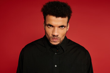 Fototapeta premium A young man exudes charm and confidence in a black shirt with a striking red backdrop.