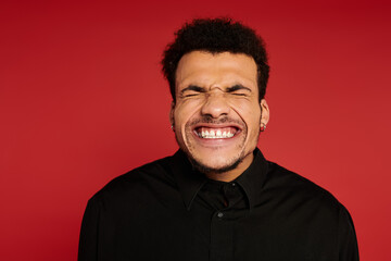 Obraz premium A young handsome man with a joyful expression stands with a red backdrop, radiating positivity.