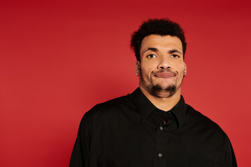 Fototapeta premium Young handsome man stands with a relaxed expression in front of a bold red backdrop.