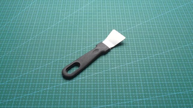 Hand placing plastic-handled metal scraper on green self-healing cutting mat for crafting or model-making