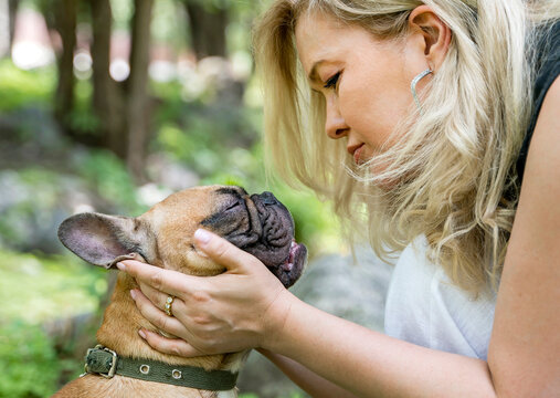 Affectionate woman holding adorable French bulldog in peaceful nature