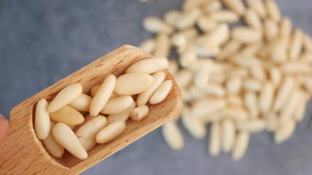 Pine nuts in wooden scoop with pile of nuts in background, static camera