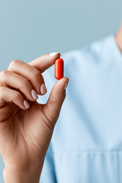 Close up of a medical worker holding a bright red pill capsule.