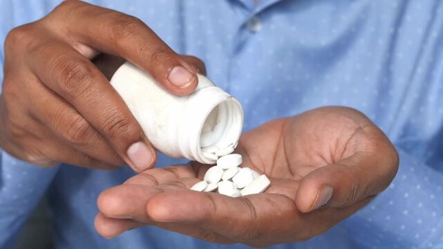 Close up male hands pouring white pills from bottle into palm showing medical concept and medication dosage in motion footage