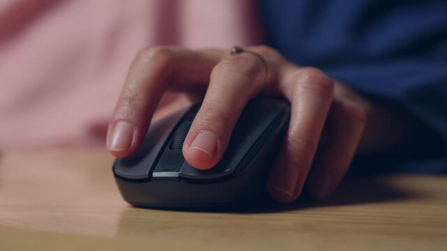 woman hand grips and clicking mouse on wooden desk, night setting