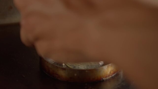 person cracked egg into a metal ring holds a sunny-side-up egg on a hot flat griddle