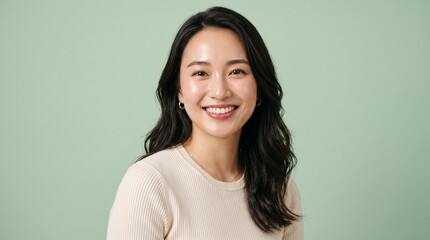 Fototapeta premium Portrait of a smiling young Asian woman with healthy glowing skin posing against a light green studio background