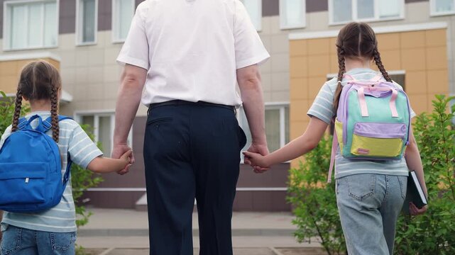 happy family, happy father takes girls child kid school lesson, first-graders school backpacks walk with dad park, background school building, child holds hand parent man father, first-graders student