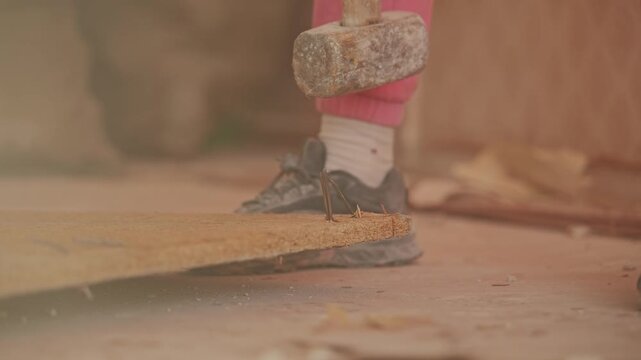 Slow motion reveals powerful hammer strike bending stubborn floor nail with dust