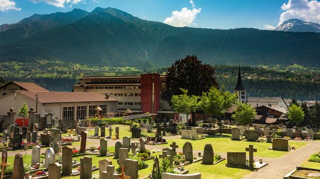 Brig Switzerland cemetery time lapse with rushing clouds over alpine mountains and sunlit headstones on a bright summer day