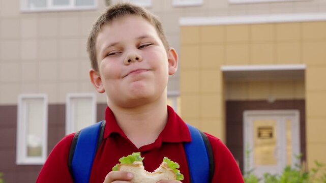Happy boy with sandwich, smiling kid outside school, cheerful student holding lunch, first day of school excitement, enjoying lunchtime outdoors, fresh sandwich with lettuce, confident expression, red