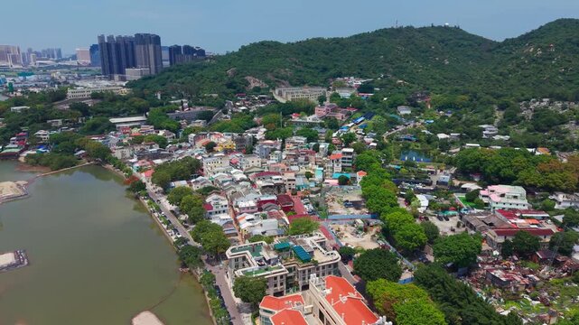 Aerial flyover reveals Coloane Village colorful rooftops beside canal with Cotai Strip casino skyscrapers rising across bay in distance
