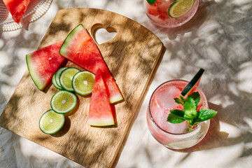 Obraz premium Summer refreshing watermelon drink with ice, mint and slices of lime on the table in the garden. Fresh healthy cold melon beverage. Fruit infused water, herbs and lemon.