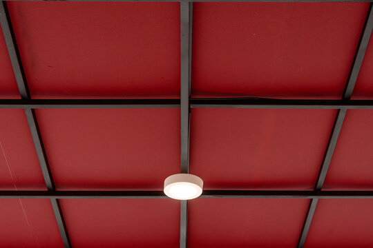Red ceiling with black metal grid framing and round white light fixture.