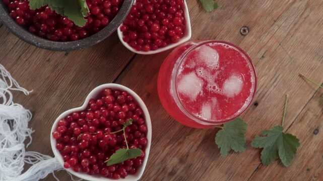 Close-up of heart shaped white bowl overflowing with fresh red currants placed beside glass jug of currant drink on rustic wooden table, evoking homemade freshness.