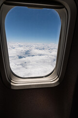 Naklejka premium Airplane Window View Above Clouds and Snow-Capped Mountains